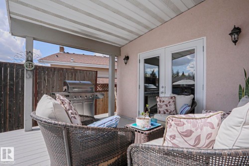 Covered outdoor deck with white painted wood-finish flooring, featuring a stucco exterior wall and white-framed double French doors - 1214 85 Street Nw, Edmonton, AB - Outdoor With Deck Patio Veranda With Exterior