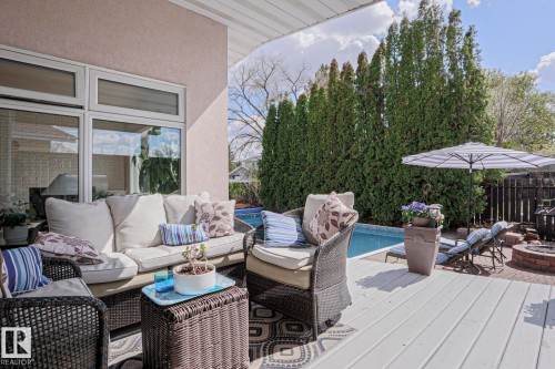 Expansive backyard deck featuring grey planking, a built-in swimming pool, a brick fire pit, and a privacy hedge - 1214 85 Street Nw, Edmonton, AB - Outdoor With Deck Patio Veranda With Exterior