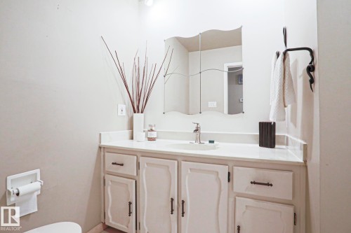Bathroom vanity featuring a single basin sink set in a light-toned countertop, white cabinetry with dark hardware, and a decorative wall mirror - 1214 85 Street Nw, Edmonton, AB - Indoor Photo Showing Bathroom
