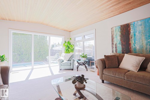 Spacious living area featuring a light-colored wood-paneled ceiling, large sliding glass doors, multiple windows, and light-toned carpeting - 1214 85 Street Nw, Edmonton, AB - Indoor Photo Showing Living Room