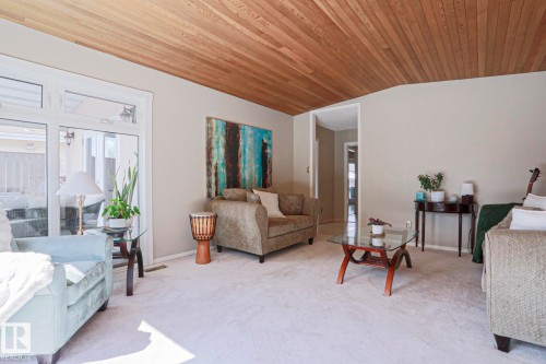 Living area featuring a wood-panel ceiling, light neutral wall paint, and light-colored carpeting - 1214 85 Street Nw, Edmonton, AB - Indoor