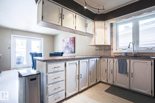 Kitchen featuring wood-finish flooring, white cabinetry with silver-tone hardware, a dark countertop, and a tiled backsplash - 1214 85 Street Nw, Edmonton, AB - Indoor Photo Showing Kitchen