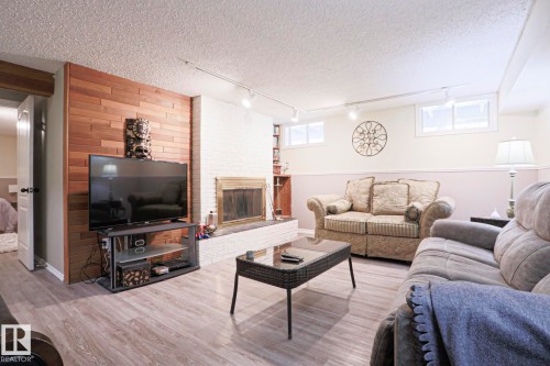Living area featuring wood-finish flooring, a white brick fireplace with a brass-toned insert, and a wood-paneled accent wall - 1214 85 Street Nw, Edmonton, AB - Indoor Photo Showing Living Room