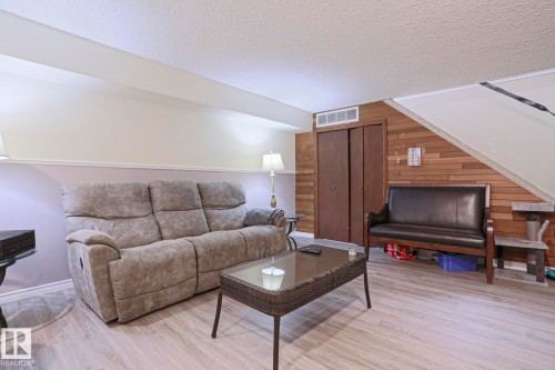 Finished room featuring wood-finish flooring, accent wall with horizontal wood paneling, and a built-in closet with bi-fold doors - 1214 85 Street Nw, Edmonton, AB - Indoor Photo Showing Living Room