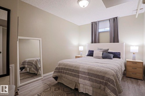 Bedroom featuring light neutral wall tones, wood-finish flooring, a window with blinds and curtain rod, an overhead flush-mount light fixture, and white baseboards - 1214 85 Street Nw, Edmonton, AB - Indoor Photo Showing Bedroom