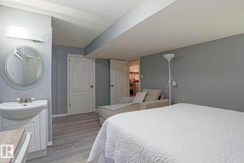 Pedestal sink vanity with a circular mirror and overhead bar lighting - 1214 85 Street Nw, Edmonton, AB - Indoor Photo Showing Bedroom