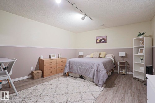 Interior room with wood-finish flooring, two-tone painted walls with chair rail trim, and track lighting - 1214 85 Street Nw, Edmonton, AB - Indoor Photo Showing Bedroom