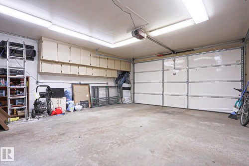 Attached garage featuring a sectional overhead door, overhead fluorescent lighting, and extensive wall-mounted cabinetry - 1214 85 Street Nw, Edmonton, AB - Indoor Photo Showing Garage