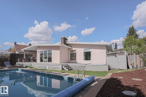 Expansive backyard featuring a rectangular swimming pool with integrated steps, a multi-level wood deck, a covered patio area, and a stucco exterior - 1214 85 Street Nw, Edmonton, AB - Outdoor With In Ground Pool