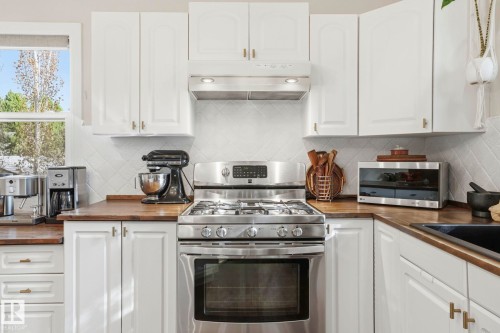 Stainless steel gas range with coordinating ventilation hood, white cabinetry, wood-finish countertops, geometric tile backsplash, and a corner sink - 4 Langley Dr, Fort Saskatchewan, AB - Indoor Photo Showing Kitchen