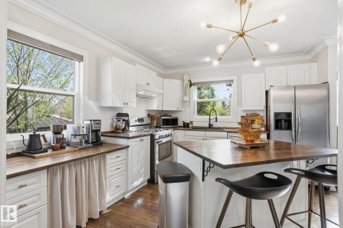 Bright kitchen featuring white shaker cabinetry, stainless steel appliances, wood-finish countertops, and an island with seating - 4 Langley Dr, Fort Saskatchewan, AB - Indoor Photo Showing Kitchen
