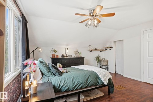 Attic bedroom featuring angled ceilings, wood-finish flooring, a contemporary ceiling fan with integrated lighting, and a window with a brick accent wall - 4 Langley Dr, Fort Saskatchewan, AB - Indoor Photo Showing Bedroom