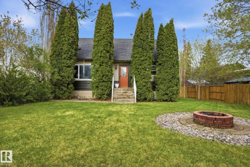 Expansive lawn area featuring a brick fire pit with a stone and paver surround - 4 Langley Dr, Fort Saskatchewan, AB - Outdoor