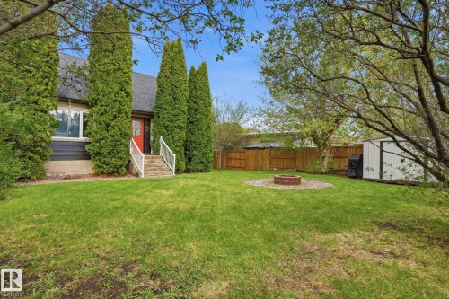 Expansive backyard featuring a manicured lawn, established trees, a built-in fire pit with gravel surround, a functional storage shed, and privacy fencing - 4 Langley Dr, Fort Saskatchewan, AB - Outdoor
