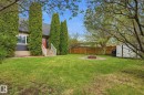 Expansive backyard featuring a manicured lawn, established trees, a built-in fire pit with gravel surround, a functional storage shed, and privacy fencing - 4 Langley Dr, Fort Saskatchewan, AB  - Outdoor 