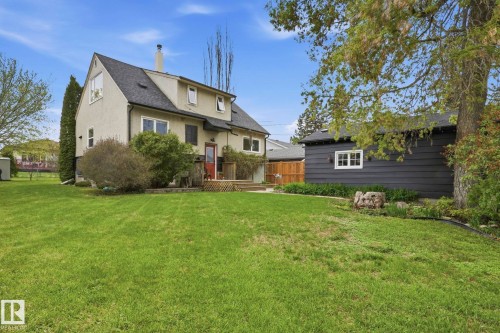 Expansive green lawn with a stucco-clad residence featuring a dormer window, a chimney, and a wooden deck - 4 Langley Dr, Fort Saskatchewan, AB - Outdoor