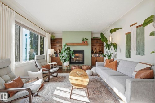 Living area featuring a fireplace with a wood mantle, built-in shelving, large window, and light-toned walls - 4 Langley Dr, Fort Saskatchewan, AB - Indoor Photo Showing Living Room With Fireplace