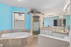 Bathroom featuring a built-in soaking tub, dual glass vessel sinks, an enclosed shower with a gold-tone frame, and extensive mirror coverage - 