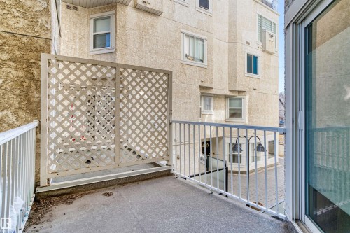 Balcony with concrete flooring and white metal railings, featuring a lattice privacy screen and a sliding glass door entry - 205 10939 82 Avenue, Edmonton, AB - Outdoor With Exterior