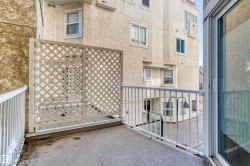 Balcony with concrete flooring and white metal railings, featuring a lattice privacy screen and a sliding glass door entry - 