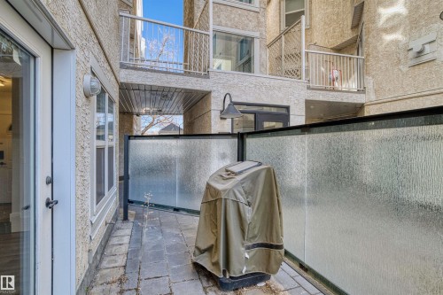 Exterior patio featuring textured privacy screening, paver flooring, and direct access through a glass-paneled door - 205 10939 82 Avenue, Edmonton, AB - Outdoor With Exterior