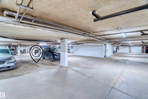 Covered parking garage featuring concrete flooring, exposed overhead piping, column supports, and fluorescent lighting - 205 10939 82 Avenue, Edmonton, AB - Indoor Photo Showing Garage
