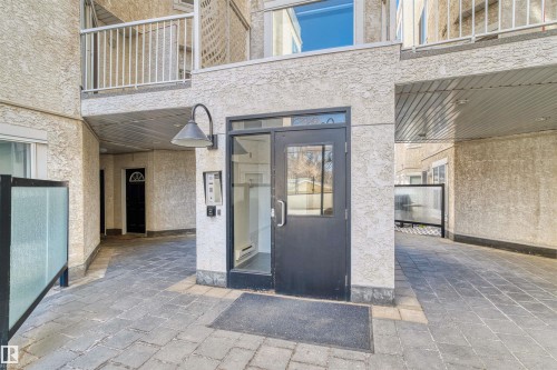 Ground-level entry featuring a dark-toned door with window inserts, a wall-mounted light fixture, and an intercom system - 205 10939 82 Avenue, Edmonton, AB - Outdoor With Exterior