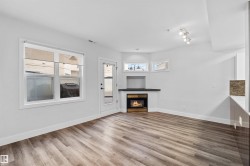 Spacious room featuring wood-finish flooring, a built-in fireplace with a dark mantel, multiple windows, and a glass-paned door - 