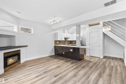 Open-concept living area featuring wood-finish flooring, a built-in fireplace, and a kitchen island with seating - 205 10939 82 Avenue, Edmonton, AB - Indoor With Fireplace
