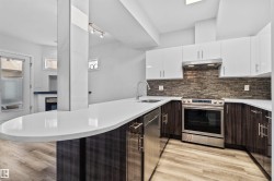 Contemporary kitchen featuring an expansive countertop island with an integrated sink and stainless steel faucet, two-tone cabinetry, a tile backsplash, and stainless steel appliances - 