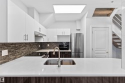 Modern kitchen featuring white cabinetry, a built-in stainless steel range hood, stainless steel refrigerator, white countertops, and a textured backsplash - 