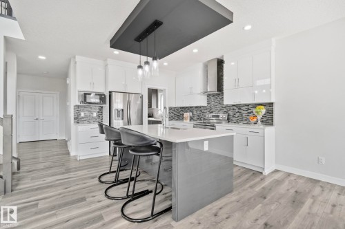 Modern kitchen featuring a central island with a light-toned countertop and seating for three - 334 Aston Close, Leduc, AB - Indoor Photo Showing Kitchen With Upgraded Kitchen