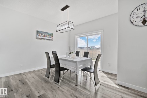 Spacious dining area featuring wood-finish flooring, a modern linear chandelier, and a sliding glass door providing exterior access - 334 Aston Close, Leduc, AB - Indoor Photo Showing Dining Room