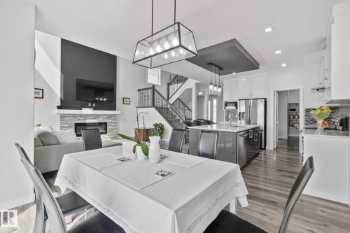 Open-concept living space featuring wood-finish flooring, a contemporary fireplace with a stone surround, and a kitchen island with pendant lighting - 334 Aston Close, Leduc, AB - Indoor Photo Showing Dining Room