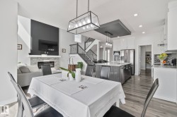 Open-concept living space featuring wood-finish flooring, a contemporary fireplace with a stone surround, and a kitchen island with pendant lighting - 