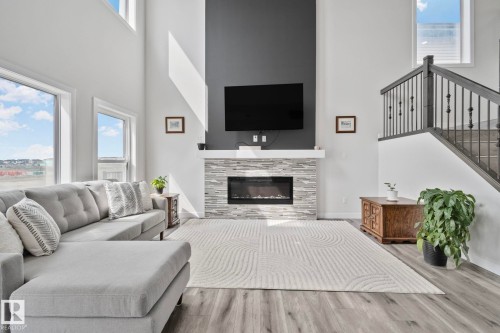 Two-story living area featuring a stone-faced fireplace with mantle, wood-finish flooring, high ceilings, and large windows - 334 Aston Close, Leduc, AB - Indoor Photo Showing Living Room With Fireplace