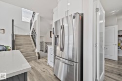 Modern kitchen area featuring a stainless steel refrigerator, white cabinetry, and a light-toned countertop - 
