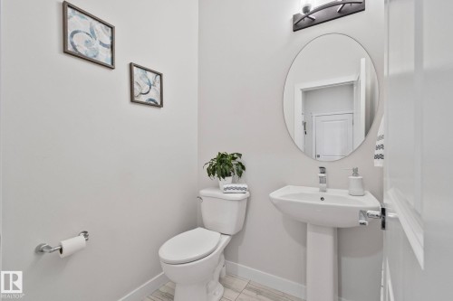 Bright powder room featuring a pedestal sink, oval vanity mirror, and contemporary wall sconce - 334 Aston Close, Leduc, AB - Indoor Photo Showing Bathroom