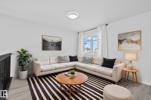 Living area featuring wood-finish flooring, a contemporary ceiling light fixture, a window with white curtains, and a black wrought iron railing - 334 Aston Close, Leduc, AB - Indoor Photo Showing Living Room