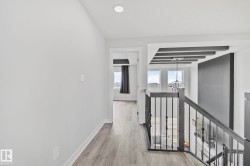 Upper-level hallway featuring wood-finish flooring, recessed lighting, and a doorway leading to an additional space - 