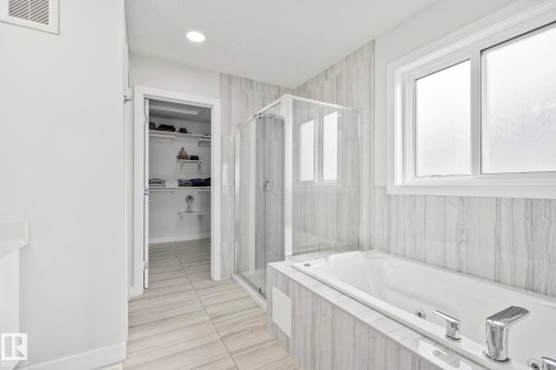 Spacious bathroom featuring a soaking tub with integrated jets, a glass-enclosed shower, and a walk-in closet with built-in shelving - 334 Aston Close, Leduc, AB - Indoor Photo Showing Bathroom