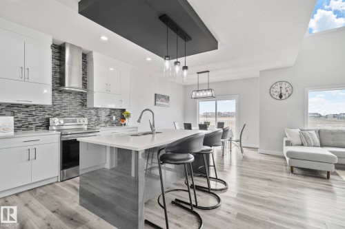 Modern kitchen featuring light cabinetry, stainless steel appliances, a mosaic tile backsplash, and a central island with a sink and seating - 334 Aston Close, Leduc, AB - Indoor Photo Showing Kitchen With Upgraded Kitchen