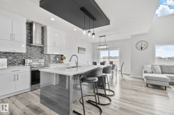 Modern kitchen featuring light cabinetry, stainless steel appliances, a mosaic tile backsplash, and a central island with a sink and seating - 