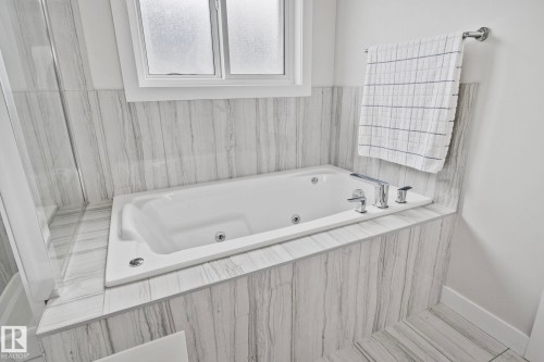 White soaking tub with integrated jets, chrome fixtures, and a frosted window - 334 Aston Close, Leduc, AB - Indoor Photo Showing Bathroom