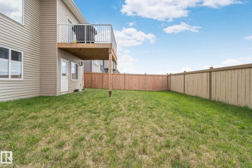 Expansive backyard featuring a fenced perimeter, a rear entrance door, and a second-story wooden deck with white railings - 334 Aston Close, Leduc, AB - Outdoor