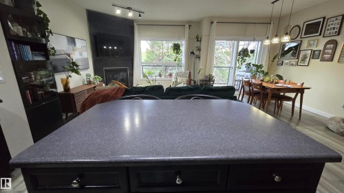 Central kitchen island featuring a dark speckled countertop and cabinet storage - 90 3010 33 Avenue, Edmonton, AB - Indoor Photo Showing Dining Room With Fireplace