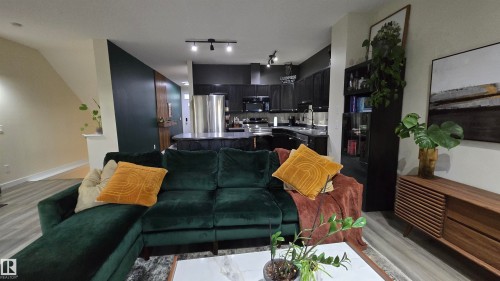 Open-concept living space featuring wood-finish flooring, a contemporary kitchen with dark cabinetry, stainless steel appliances, and track lighting - 90 3010 33 Avenue, Edmonton, AB - Indoor Photo Showing Living Room