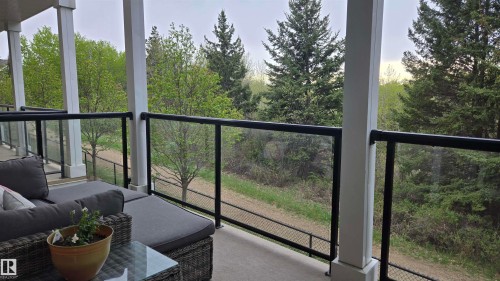 Covered outdoor deck with glass panel railings and white support columns, overlooking mature trees and natural landscaping - 90 3010 33 Avenue, Edmonton, AB -  With Exterior