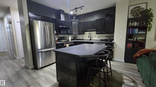 Kitchen featuring dark cabinetry, stainless steel appliances, an island with countertop seating, and light wood-finish flooring - 90 3010 33 Avenue, Edmonton, AB - Indoor Photo Showing Kitchen With Stainless Steel Kitchen