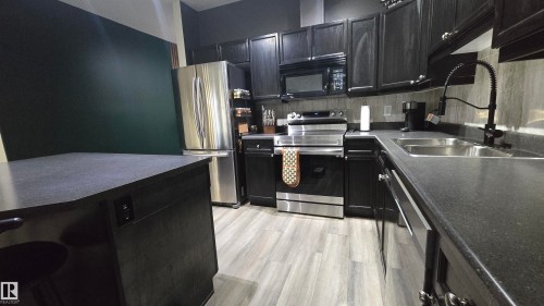 Kitchen featuring dark cabinetry, stainless steel appliances, and wood-finish flooring - 90 3010 33 Avenue, Edmonton, AB - Indoor Photo Showing Kitchen With Stainless Steel Kitchen With Double Sink